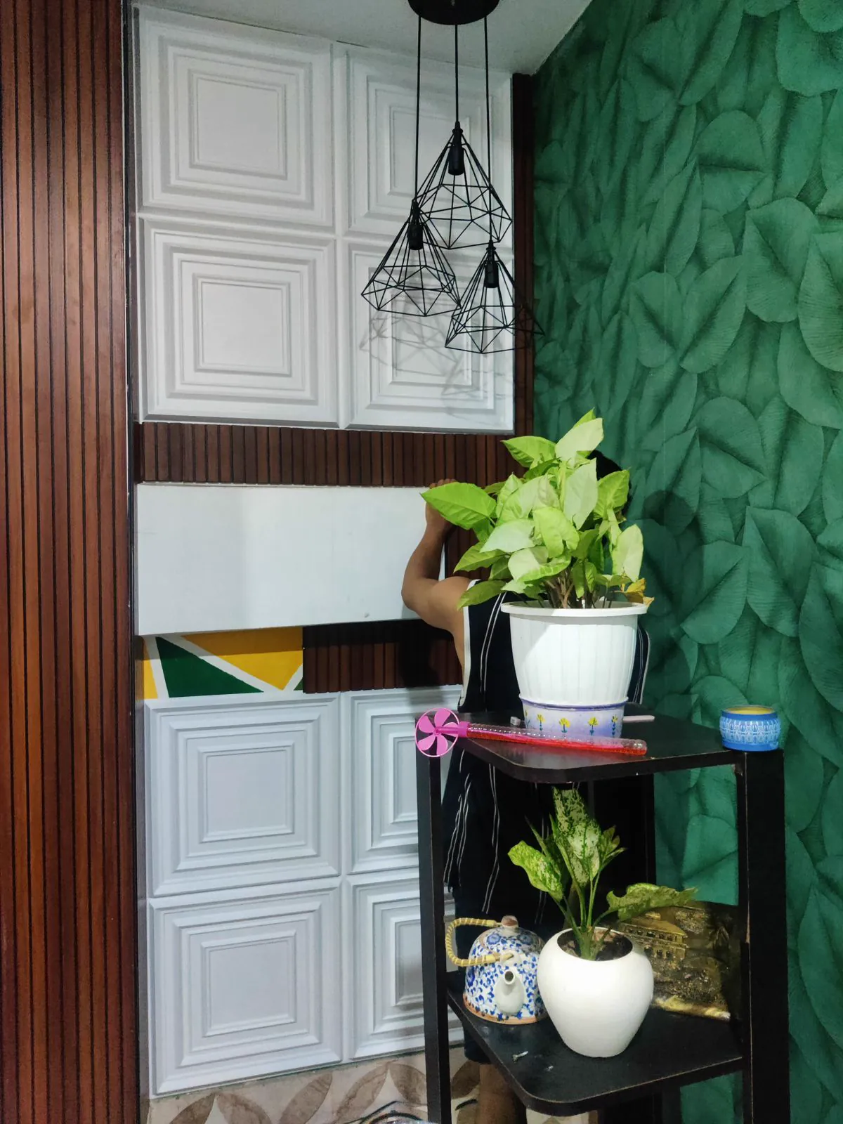 Corner with white coffered foam tiles going up beside a deep green embossed leaf wallpaper